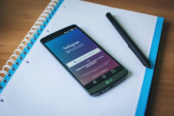 A phone displaying Instagram's login page on top of a notebook next to a pen demonstrating social media management